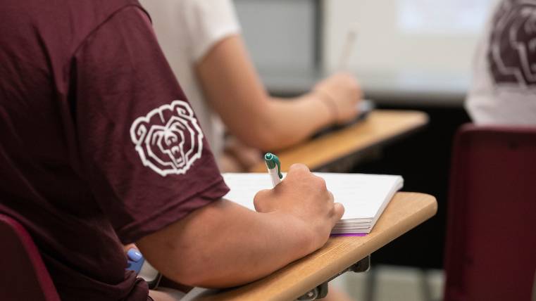 A Missouri State student takes notes with a Bear Head logo on their maroon shirt
