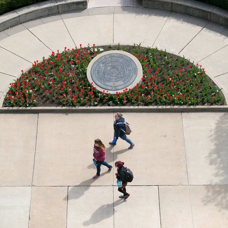 Three students walk past the seal of the university
